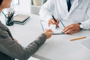 a doctor writes on a clipboard while a person asks about addiction treatment and insurance coverage