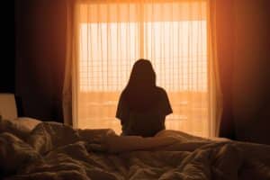 a person with co-occurring disorders and addiction looks out of a window in a dark room