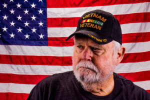 a vietnam veteran stands in front of a flag possibly aware of the link between veterans and addiction risk