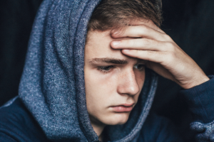 a young person holds their head, possibly a victim of the link between children and opioid poisoning