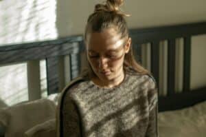 woman with her hair in a half bun sitting on her bed in front of a wall