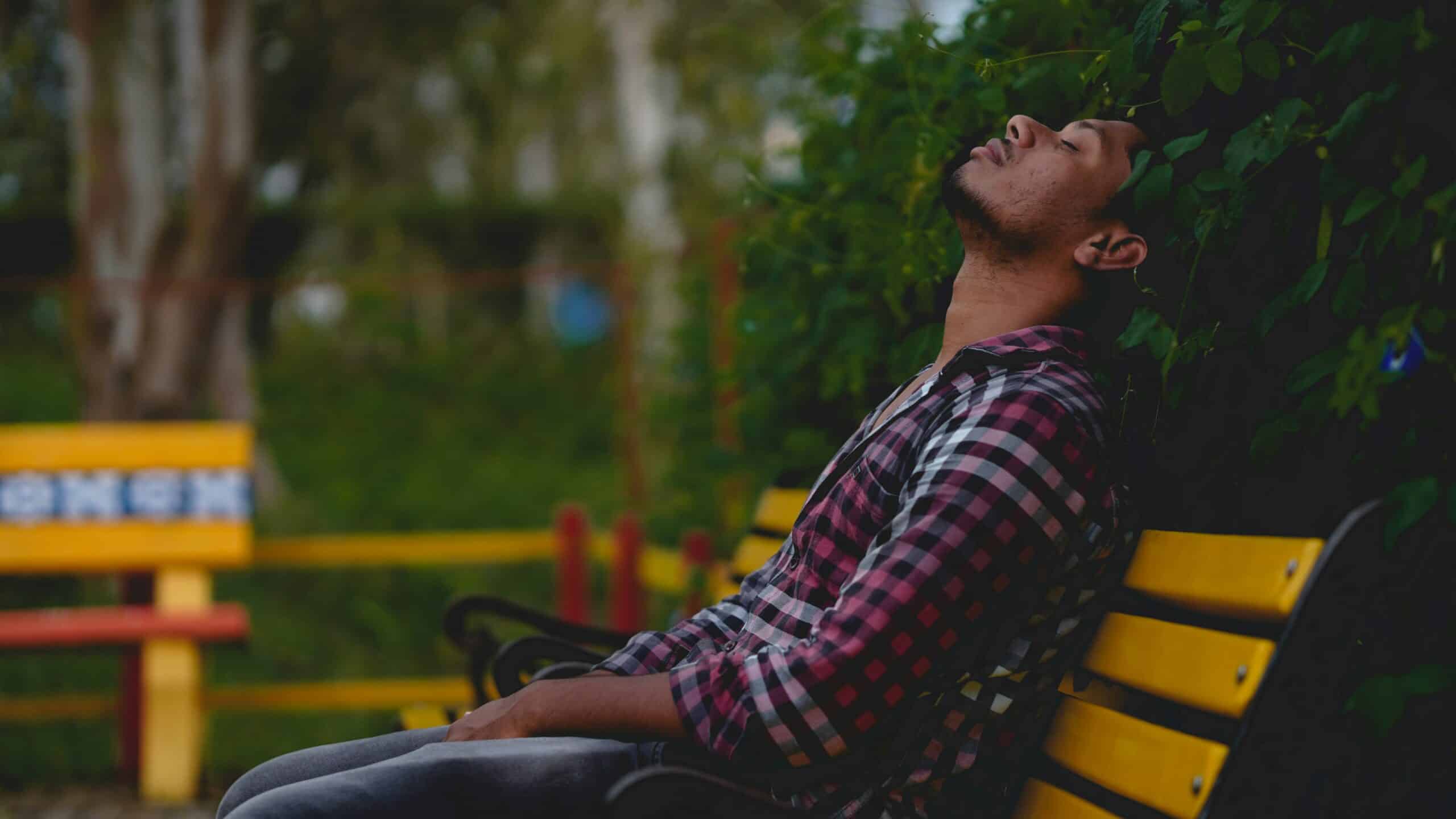man with high functioning depression sitting on a bench at a park with his eyes closed and head tilted back