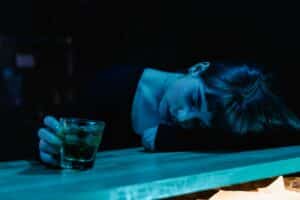 A woman sleeping on a bar with an alcoholic drink in her hand while she contemplates the signs it's time to quit drinking
