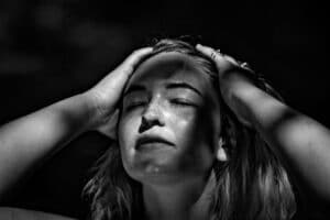 Emotional woman with hands in her hair and face exposed to the sky and eyes closed.