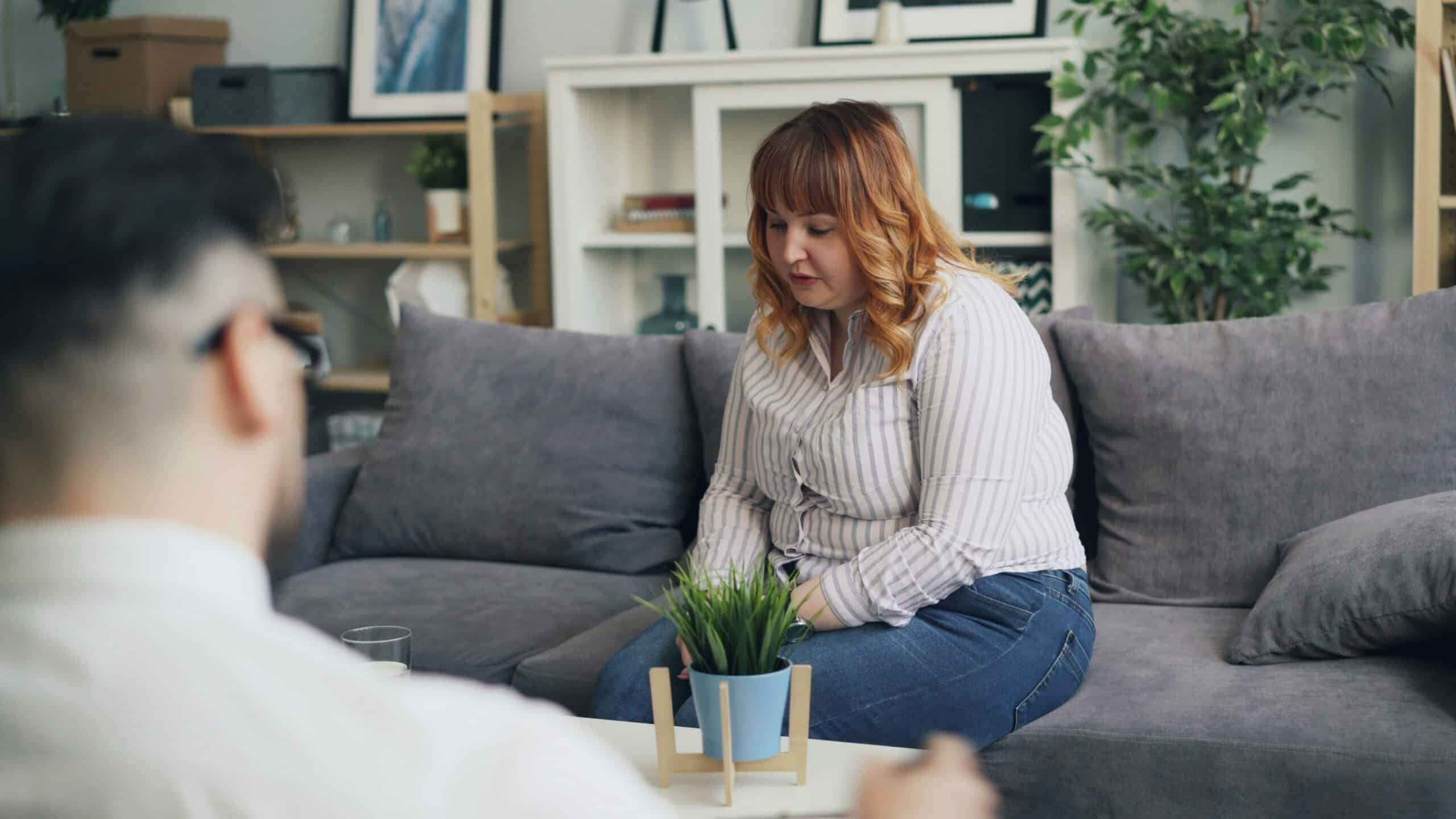 gay woman with red hair and bangs sitting on gray couch receiving therapy