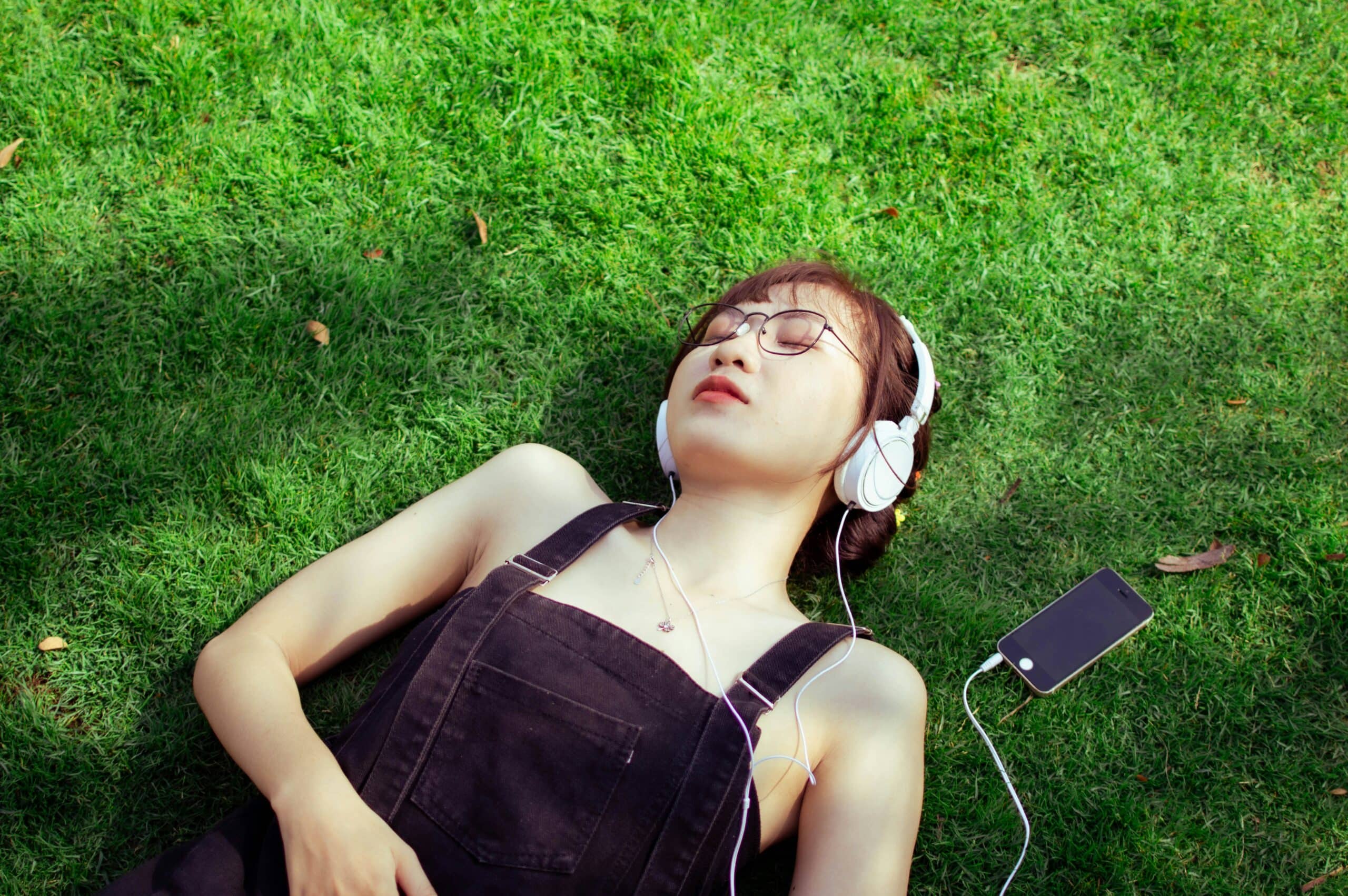 woman laying on the grass outside, closing her eyes while listening to music as a form of therapy in addiction recovery